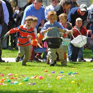 一群拿着复活节篮子的孩子跑过铺满塑料蛋的草坪，他们的父母在他们身后欢呼.